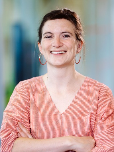 A mid-aged woman with dark hair and a red and white striped dress and round earrings has her arms crossed and smiles into the camera.